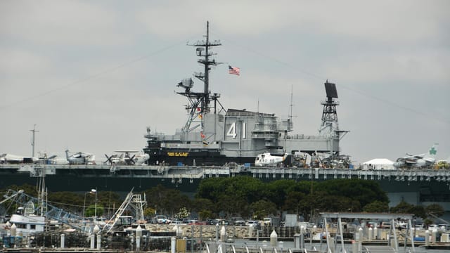 USS Midway Museum aircraft carrier docked in harbor with planes onboard and flag flying.