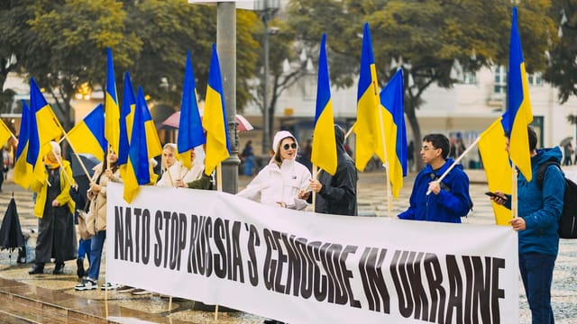 Group of people protesting against Russian actions in Ukraine with Ukrainian flags in Portugal.
