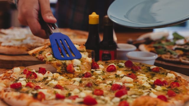 A delicious pizza slice with veggies served with a spatula indoors.