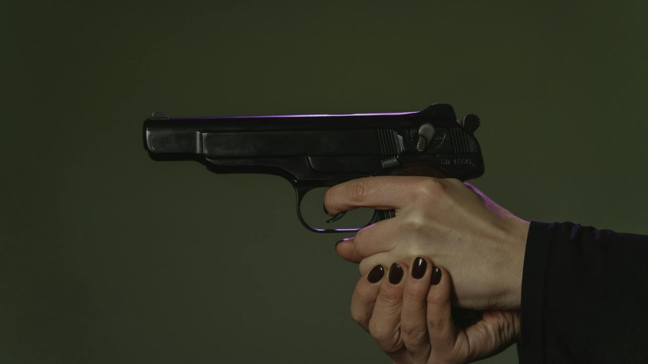 A detailed shot of hands holding a black handgun with dark painted nails.