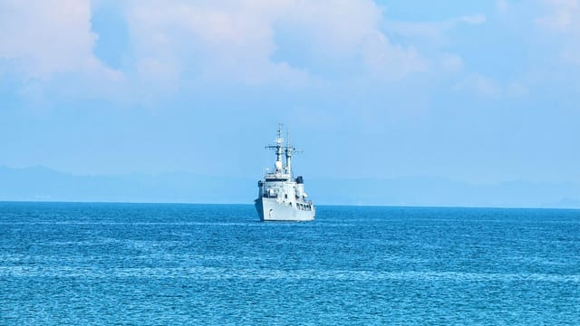 A naval vessel sailing across a calm blue ocean under a clear sky.