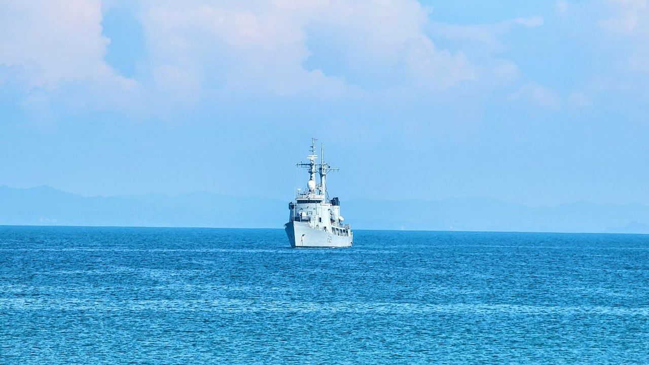 A naval vessel sailing across a calm blue ocean under a clear sky.