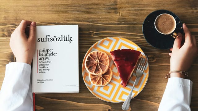 A top view of coffee, cake, and a book on a wooden table, creating a cozy breakfast scene.