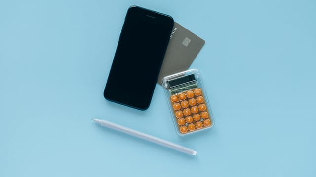 A modern flat lay of a smartphone, credit card, and calculator on a blue background.