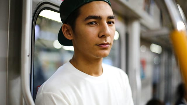 Teenager wearing a baseball cap on a train in Tokyo. Urban public transport scene.