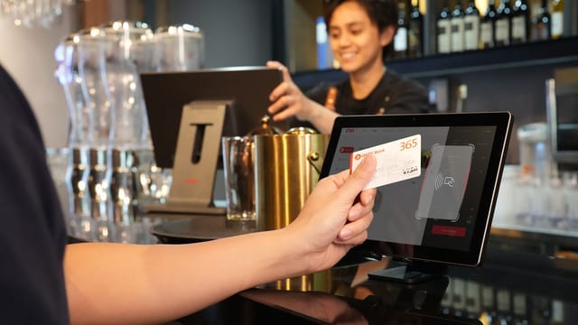 Person using contactless credit card payment at a modern bar, assisted by a cashier.