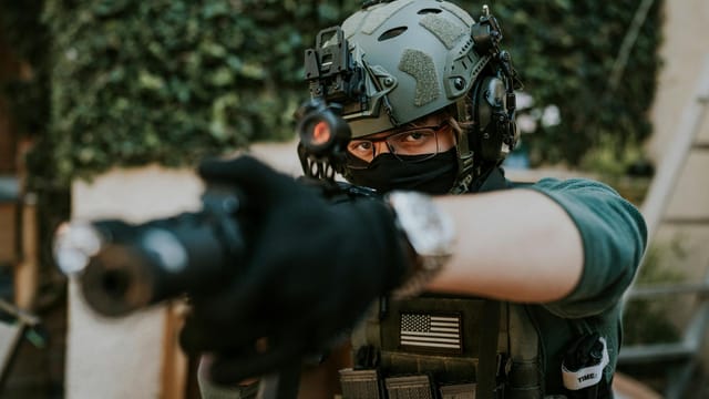 Soldier equipped with tactical gear and helmet in a ready stance outdoors.