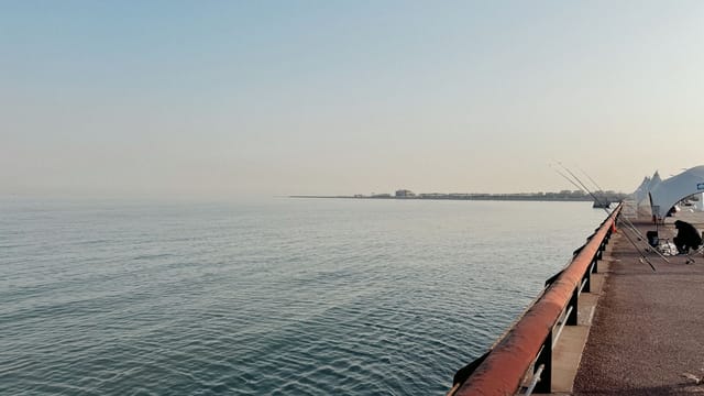 A serene view of a waterfront walkway with fishing rods set up under a clear blue sky.