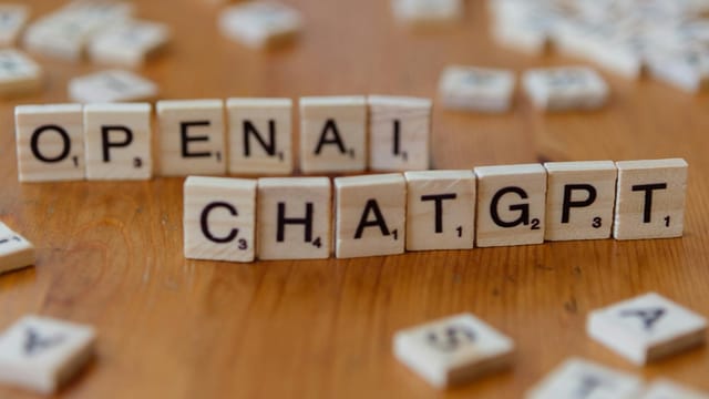 Wooden letter tiles spelling 'OPENAI CHATGPT' on a wooden surface, focused image.