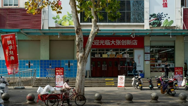 Busy street in Luoyang, China featuring bicycles, a delivery cart, and a storefront showcasing daily urban life.