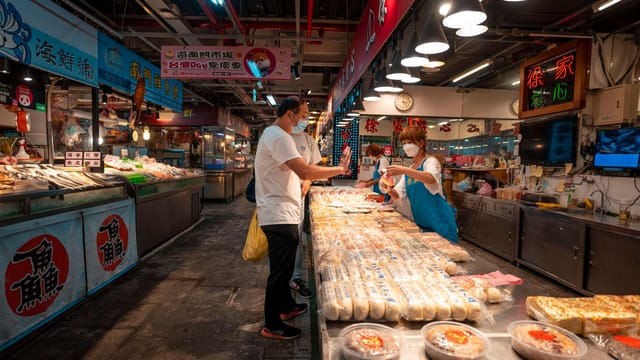 Two masked adults shopping at an indoor Asian market, choosing delicious food items.