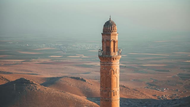 A breathtaking aerial view of a minaret in Mardin, Türkiye, during sunset, highlighting its architectural beauty.