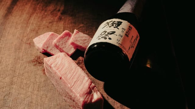 Sliced Wagyu beef paired with a bottle of premium Japanese sake, artistically presented on a wooden surface.