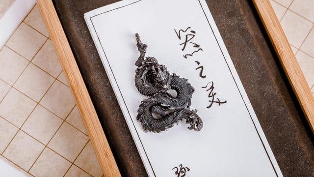 Close-up of a detailed metal dragon keychain resting on traditional Chinese calligraphy paper.