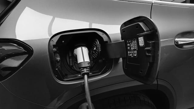 Close-up black and white image of an electric vehicle charging at a station.