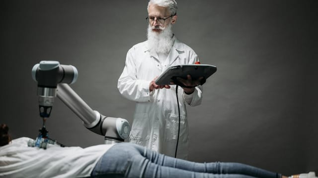 A scientist controls a robotic arm conducting research on a person lying down.