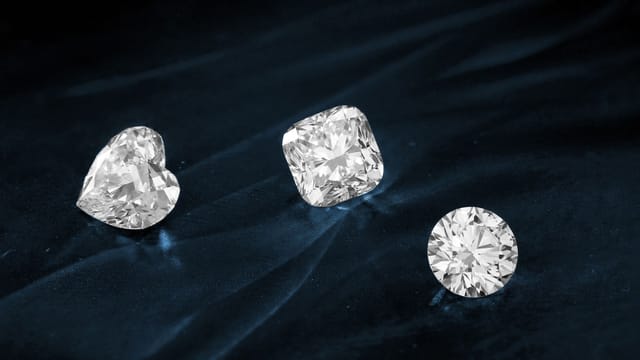 Three exquisite diamonds featuring heart, cushion, and round cuts displayed on dark fabric.