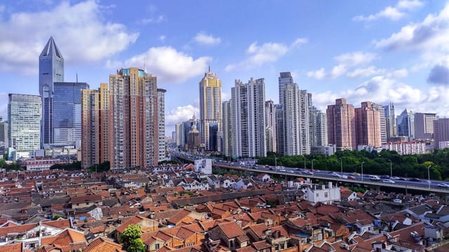 A vibrant view of Shanghai's skyline juxtaposed with traditional housing under a bright blue sky.