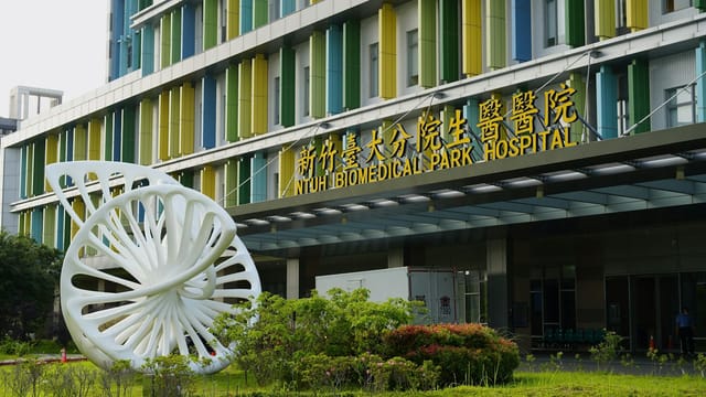 Entrance to NTUH Biomedical Park Hospital with modern sculpture and colorful facade in Taiwan.
