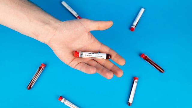 Close-up of a hand holding a blood sample vial on blue background, representing COVID-19 testing.