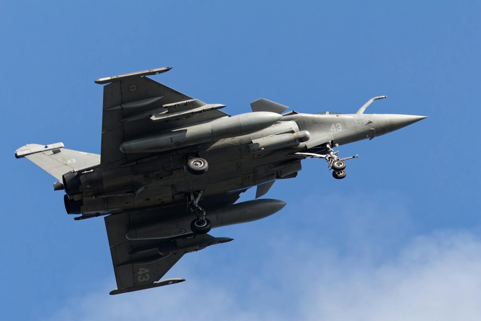 French Rafale fighter jet flying over Bretagne, France with landing gear deployed.