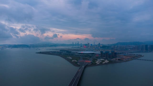 Aerial shot of a modern cityscape with waterfront view and cloudy sky at dusk.