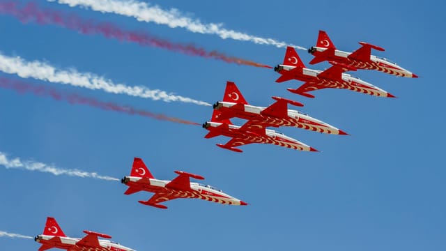 Formation of Turkish fighter jets performing aerobatic display against clear blue sky.