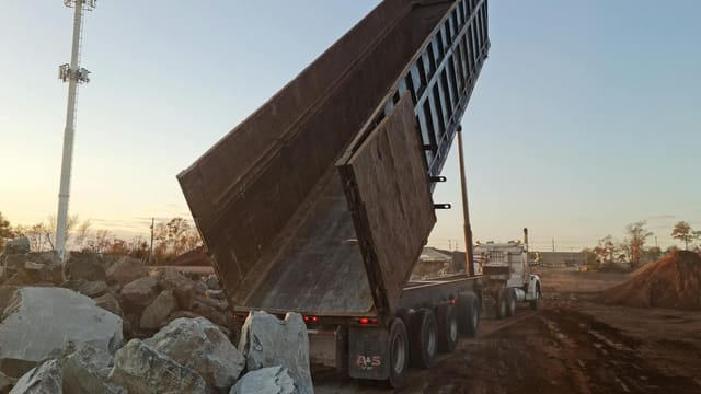A dump truck unloading rocks at a construction site during sunset.