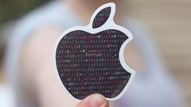 Close-up of a person holding an apple-shaped sticker with binary code, symbolizing technology.