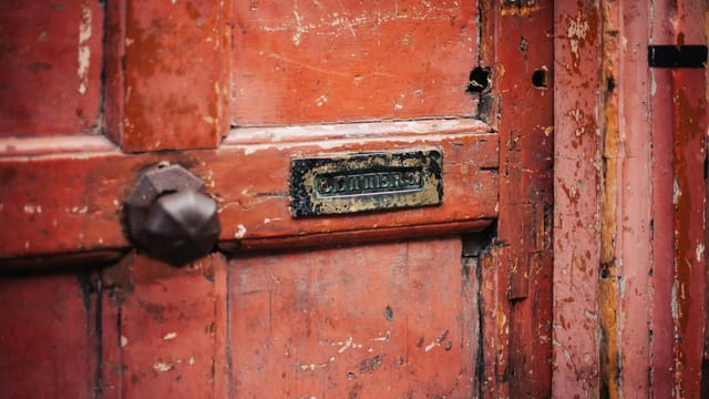 Close-up of a weathered wooden door featuring a vintage letterbox slot and peeling paint.