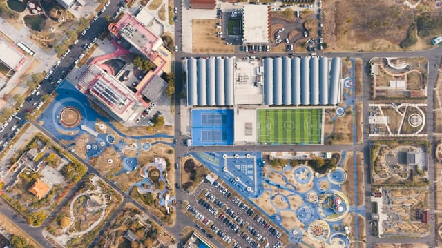 A stunning overhead shot of a sports complex with tennis courts, football field, and nearby park facilities.