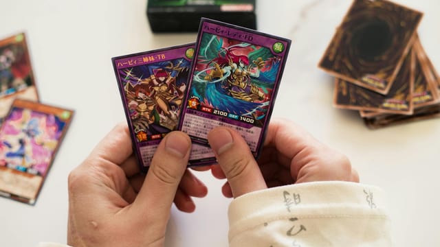 Hands holding Yu-Gi-Oh! trading cards in a dynamic gaming setup with blurred background.