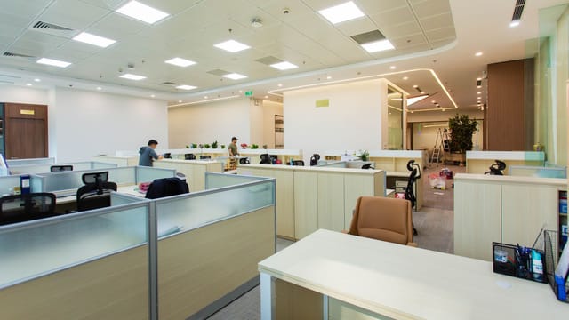 Bright and spacious office interior featuring open-plan cubicles, modern furniture, and ceiling lights.