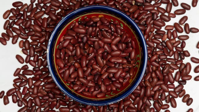 A vibrant ceramic bowl filled with red kidney beans surrounded by more beans on a white surface.