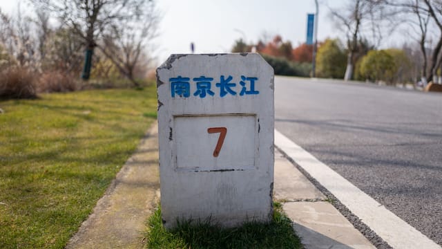 Concrete mile marker on a road in Nanjing, China, indicating distance with lush greenery around.