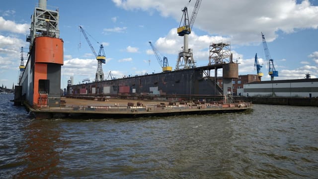 A shipyard featuring a docked vessel and multiple cranes under a bright blue sky.