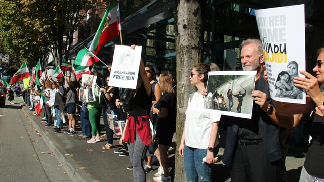 A peaceful protest in Vancouver advocating for Iranian rights with flags and placards.