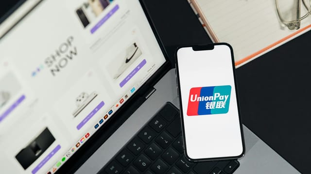UnionPay logo displayed on a smartphone next to a laptop with an online shopping page open.