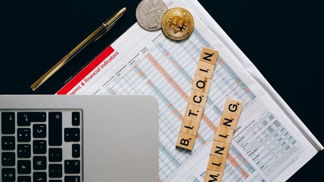 Top view of a laptop, Bitcoin coins, and financial indicators symbolizing Bitcoin mining and investment.