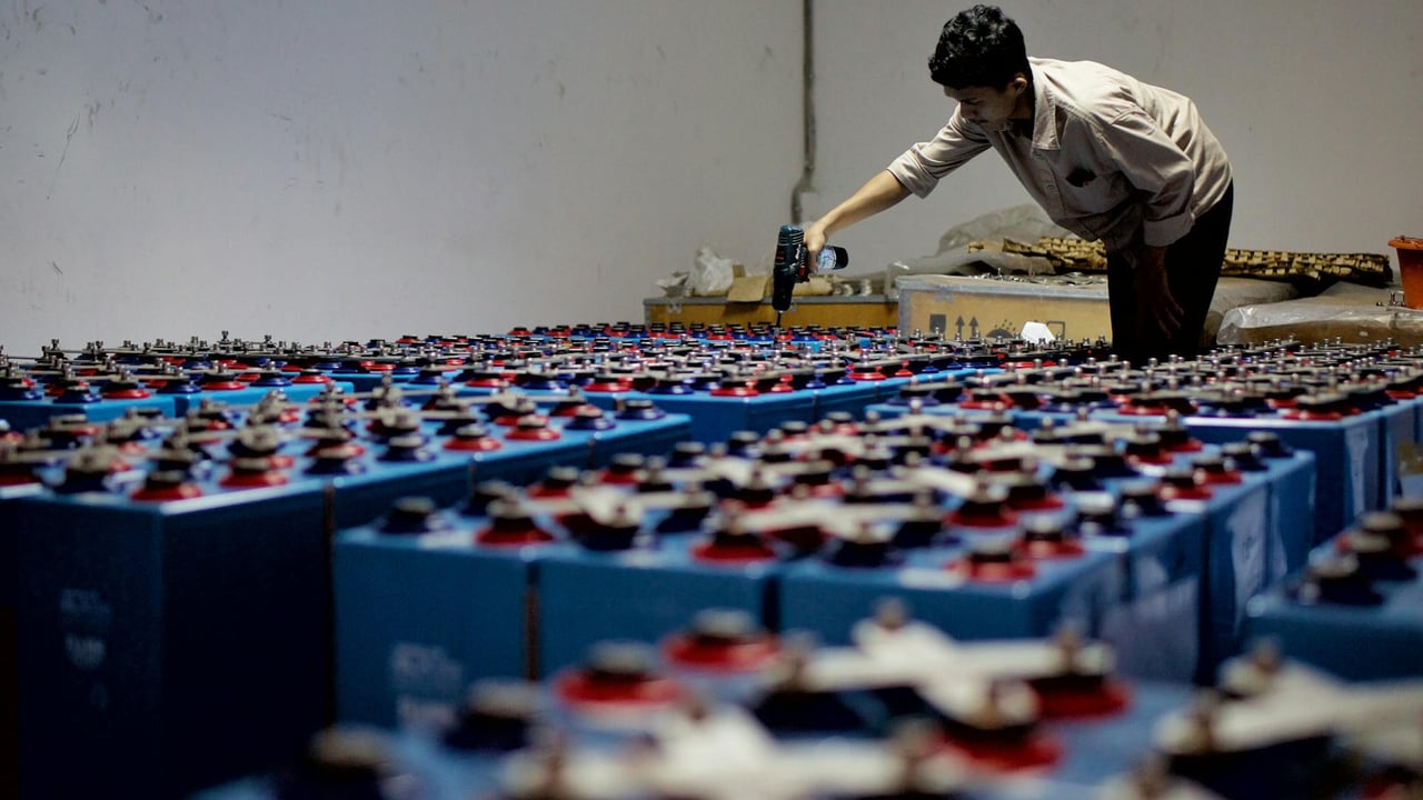 A worker checking many industrial batteries inside a facility. Indoor, industrial setting.