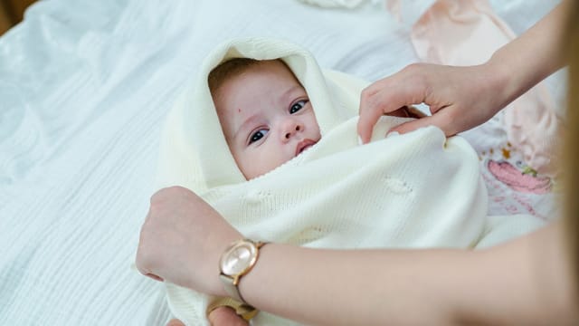 A newborn baby wrapped in a cozy cream blanket, lovingly held indoors.