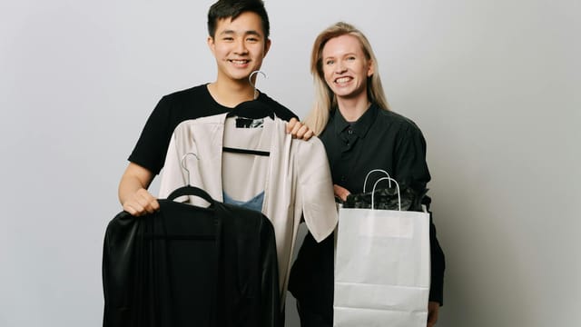A happy couple displaying fashion choices with bags and clothes in a studio setting.
