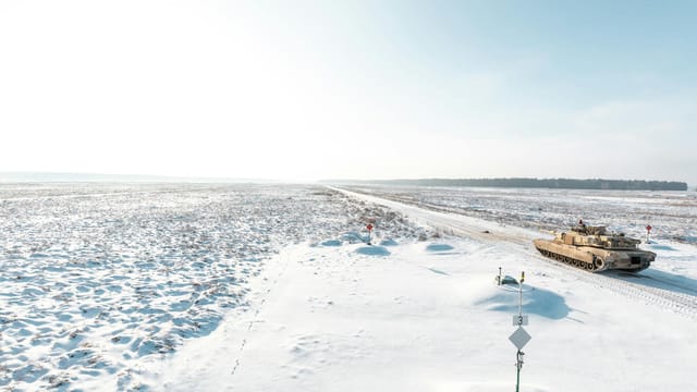 Military tank driving through a vast snow-covered terrain, conveying a scene of isolation and power.