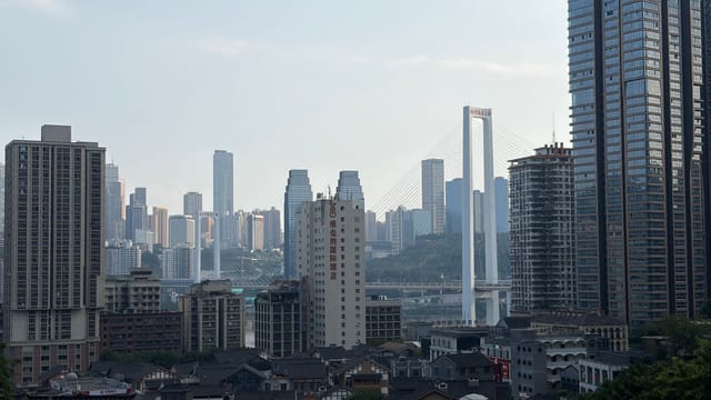 Chongqing cityscape featuring high-rise buildings and a prominent bridge under a cloudy sky.