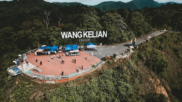 Aerial view of Wang Kelian lookout point with tourists and vendors on a sunny day.