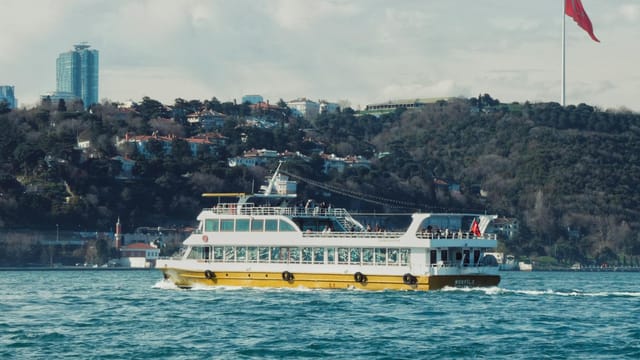 A ferry navigates the Bosphorus in Istanbul, with the iconic Turkish flag in the background.