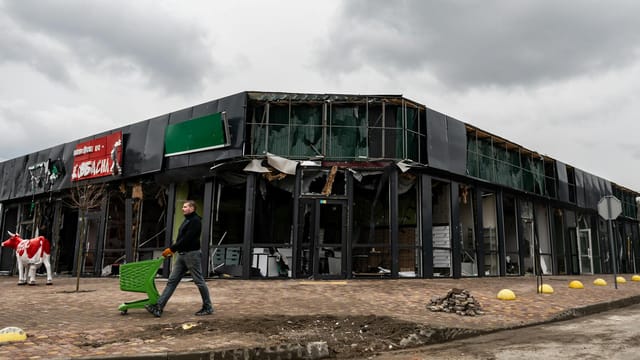 A person walks by a damaged building in Makariv, Kyiv Oblast, Ukraine, highlighting urban disaster impacts.