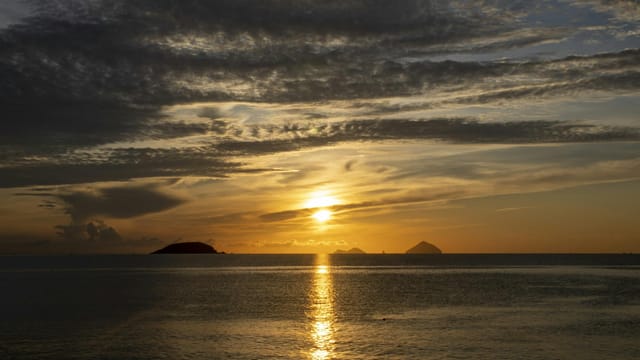 Beautiful sunset over the ocean with dramatic clouds and islands on the horizon.