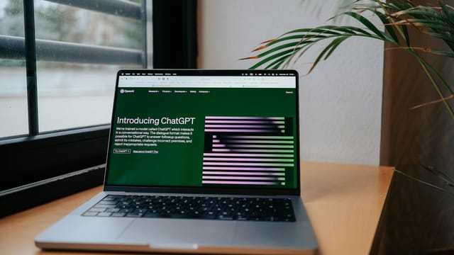A laptop displaying ChatGPT on a desk by a window, featuring a modern home office setup.