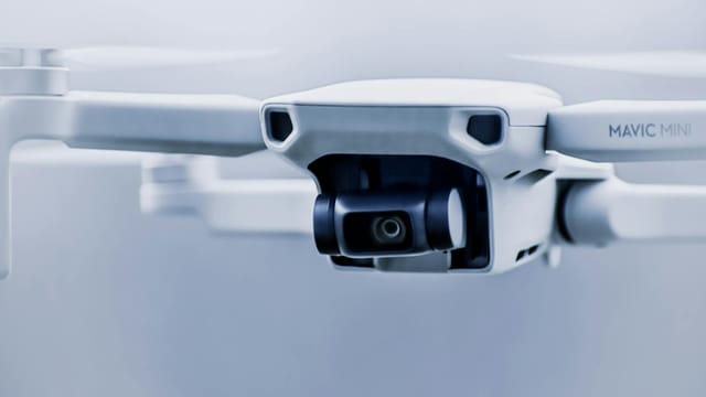Small contemporary white drone with digital camera flying in light studio against blurred background